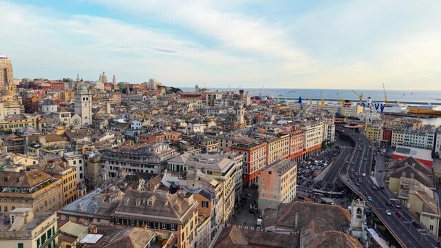 Drone push over Genoa historic center toward Porto Antico harbor at sunset, busy road with beautiful colorful architecture buildings.