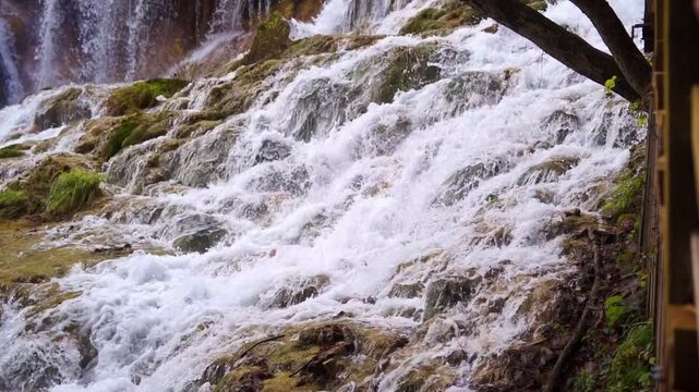 A detailed high-angle view of white-water cascades rushing over moss-covered calcified travertine rocks at the iconic Pearl Shoal Waterfall (Zhenzhu Tan Waterfall).