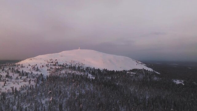 Cinematic drone shot of the first morning light hitting the snowy peak of Luosto