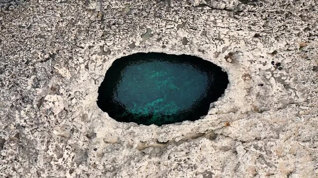 Coral Lagoon Il-Qarraba in Mellieħa Malta shows elliptical karst sinkhole carved in Upper Coralline Limestone with turquoise water pool connect to Mediterranean through submerged tunnel, aerial ascent
