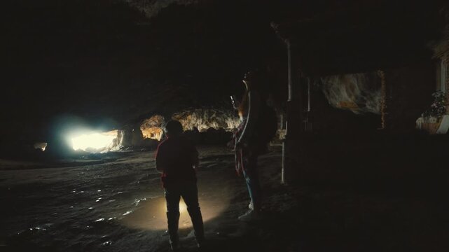 Curious boy with flashlight exploring a dark cave with his mother