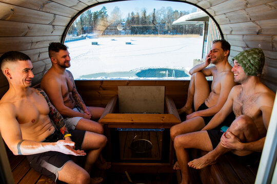 Group of happy men in barrel sauna with winter lake ice hole view, cold plunge therapy, friends enjoying thermal wellness, biohacking, sunny day