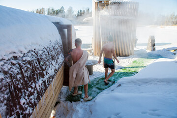 Fototapeta premium Men exiting outdoor barrel sauna in winter snow, walking to lake ice hole for cold plunge therapy, steam, nordic wellness, sunny day, biohacking