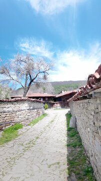 9:16 view along a bright cobblestone path leading to traditional wooden houses in Zheravna, showcasing preserved rural architecture and cultural heritage in Bulgaria.