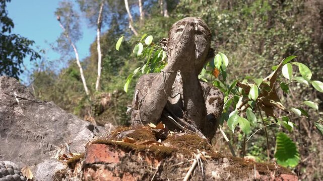 Slow circle around a stone sculpture with hands together praying, at Dragon cave in Laos.