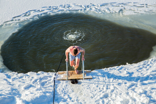 Overhead view man swimming in ice hole, cold plunge therapy, winter lake immersion, biohacking, snow texture, sun, top view, conceptual