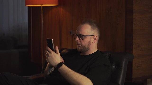 Jealous man sits on a couch and looks away from his phone, suggesting envy and emotional frustration over social media posts.