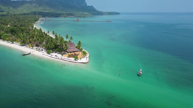 Koh Muk, Thailand: Aerial drone footage of long tail boat sailing around white sand beachfront resort of Koh Mook, an island in Andaman sea of Southern Thailand. Taken with tilt up motion on sunny day
