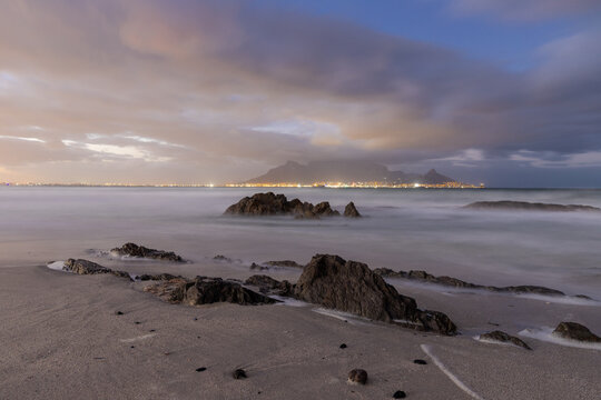 An amazing view from Bloubergstrand beach on the famous table mountain in Cape Town, seen during a colourful sunrise with a amazing dramatic cloudscape and waves braking on the coast from the rough At