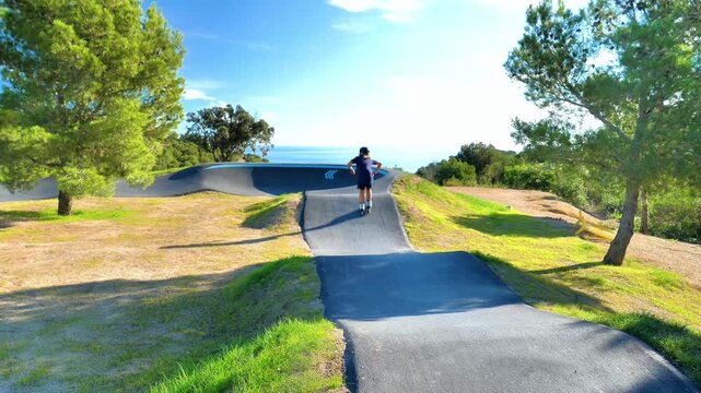 Two active children riding scooter and inline skates on a seaside pumptrack. Kids sports, brotherhood and outdoor fun concept in a sunny coastal park. Youth fitness and healthy lifestyle.