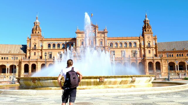 Traveler with backpack looking at the monumental fountain on Plaza de Espa&ntilde;a, Seville, Spain. Renaissance Revival architecture landmark in Andalusia at sunny day. Travel and exploration concept.