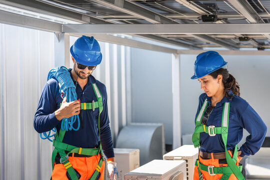 Engineers in safety harness and hardhats inspecting solar panel installation on rooftop, Sustainable energy technicians team installing solar power system on industrial building rooftop