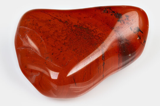 Polished jasper stone with black spots. Tumbled red jasper with glossy surface and dark flecks. Refined red jasper mineral featuring smooth contours and black specks for design
