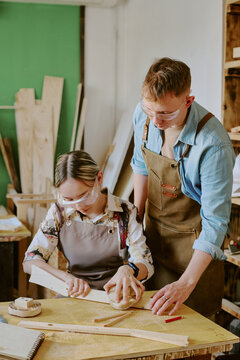Vertical shot of teenage girl woodworking with middle aged Caucasian male instructor, measuring timber in workshop. Suitable for vocational training, apprenticeship, skilled trades marketing