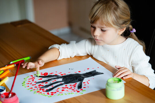 Little preschool girl painting with fingers tree on paper at home or at kindergarden daycare. Child doing creative art activity indoors. Real life, real people.