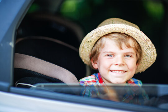 Little boy sitting in car and waving while family goes on summer road trip. Happy child enjoying travel, real life, real people.