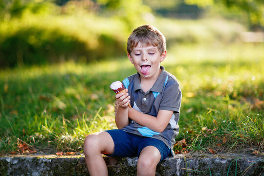 Happy little preschool boy sitting outdoors on a sunny day, smiling while eating ice cream in a park, enjoying childhood summer moments in real life.