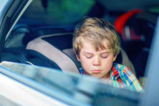 Sad little kid boy sitting in car during traffic jam on the way to summer vacation with his parents. Tired and exhausted child unhappy about the journey. Real family, real people, long car trip.