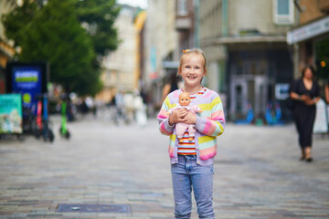 Happy young girl holding a baby doll on a pedestrian street in Helsinki, Finland, capturing...