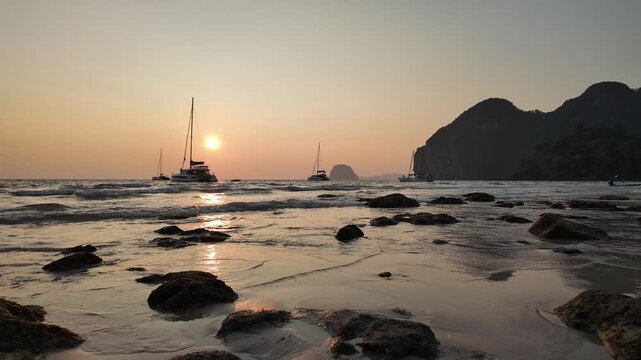 Koh Mook, Thailand: Cinematic slow motion pan footage of the sunset over Koh Muk Charlie or Farang beach with sailboats in the background in the Andaman sea in southern Thailand.
