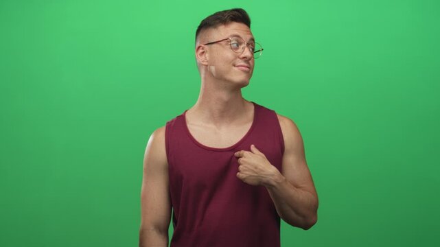 Young man in maroon tank points thumb to chest, showing bare shoulder and arm in studio; confidence playful attitude.