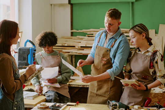 Teenagers studying woodworking, reviewing plans and taking notes during vocational class in workshop. Useful for career education, skilled trades training, apprenticeship promotion