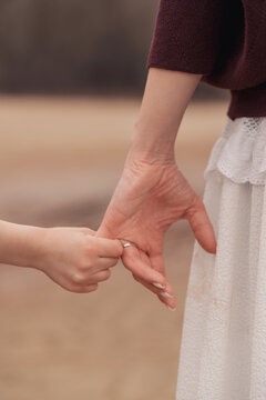 Close up of a mother and child holding hands while walking, family connection, support and trust, outdoor lifestyle.