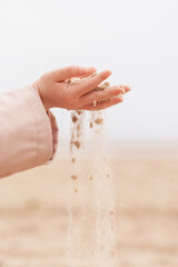 Child hands pouring dry sand on a wide beach, sensory play, childhood exploration, coastal background. © neteli