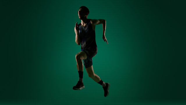 Male athlete captured in vertical jump in motion on dark green background. Concept of explosive strength, high intensity training, speed development and physical conditioning.