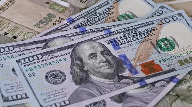 US dollar banknotes falling on Indian rupee notes. Hand throws currency over scattered 500 denomination bills. Concept of exchange rate, global finance, investment and international economy.