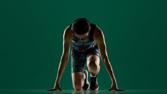 Male athlete kneeling in start position front view ready to run in studio. Concept of competition readiness visuals, focus and concentration, race start moment, performance mindset content.