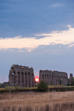 Ancient Roman aqueduct ruins in Parco degli Acquedotti Rome at sunset with wide sky and dramatic evening light over historic landscape