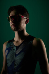 Fototapeta premium Close up portrait of male athlete wearing sports sunglasses on dark green background. Concept of sport fashion visuals, performance gear promotion, active lifestyle branding, fitness identity content.