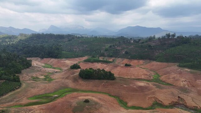 Drone shot capturing rugged landscapes in Valparai with dry soil textures, winding natural contours, scattered vegetation, and layered mountains fading into the horizon.