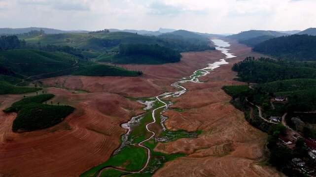 Cinematic aerial view of Sholayar Reservoir surroundings, showcasing winding mountain roads cutting through tea plantations and contrasting dry terrain, with rolling hills stretching into the distance