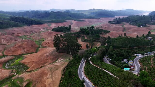 Wide cinematic aerial of Sholayar dam highlighting contrasting textures of lush plantations and dry land, with curving roads and distant hills adding depth and scale.