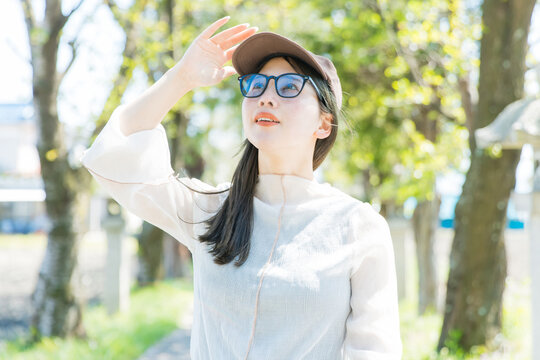 サングラスでUV対策する屋外の女性　
Young woman protecting from UV rays outdoors in park wearing sunglasses and cap sun protection portrait lifestyle