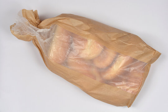 A brown paper bakery bag with a transparent plastic window filled with several golden brown bread rolls on a white background.
