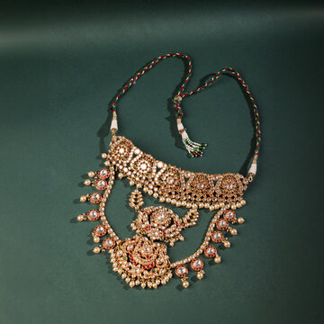 Exquisite layered Indian kundan bridal necklace set with ruby accents and white pearl drops, featuring an adjustable dori thread, elegantly displayed on a deep forest green background.