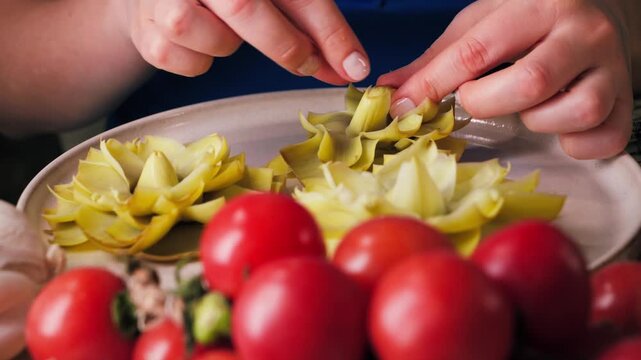 Close-up of hands opening artichoke petals and flattening the flower to prepare it for frying on both sides. The scene shows the cooking process of traditional Spanish dish las flores de alcachofa