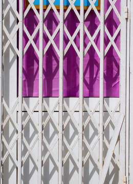 Closed shop entrance with white metal security gate casting geometric shadows on colorful background with strong contrast