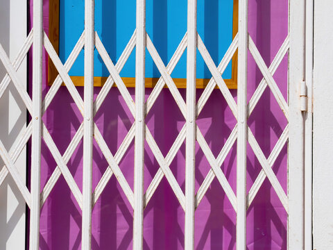 Closed shop entrance with white metal security gate casting geometric shadows on colorful background with strong contrast