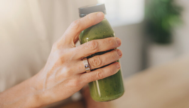 Closeup of a hand holding a green juice bottle promoting healthy lifestyle.