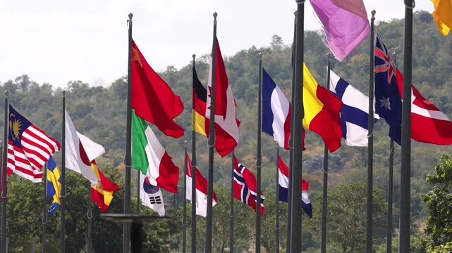 International flags waving on flagpoles against green mountain landscape background.