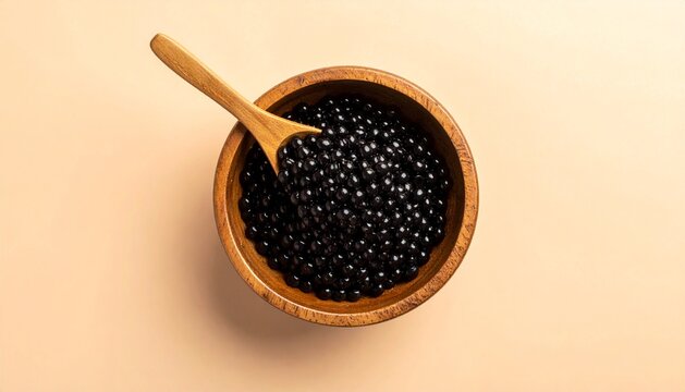 Top view of black tapioca pearls for bubble tea in a wooden bowl with a spoon on beige background