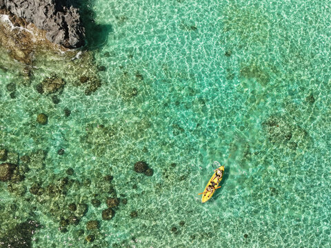 Aerial drone view of kayakers paddling through the crystal-clear turquoise waters of Big Lagoon in El Nido, Palawan, Philippines.