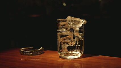 Glass Mixing Beaker Filled with Ice Cubes on Wooden Bar Counter © blueringmedia