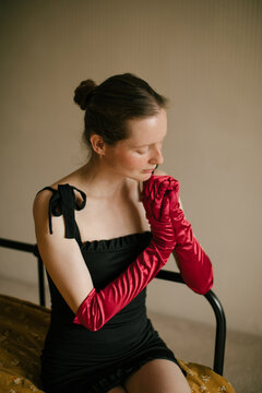 Elegant freckled woman in black dress and red gloves posing in vintage interior.