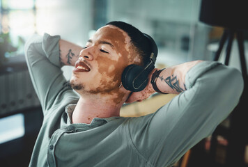 Man, headphones and relax at office with smile, relief or complete project with streaming at media company. Person with vitiligo, happy and listen to music on break, done and audio at creative agency © peopleimages.com