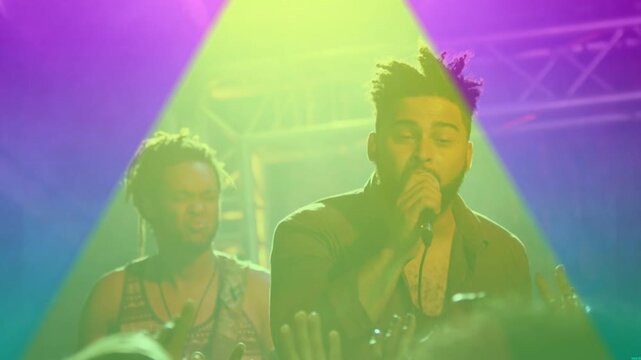 Singing lead singer in dark shirt leaning into handheld mic on stage, with colored lights shifting
